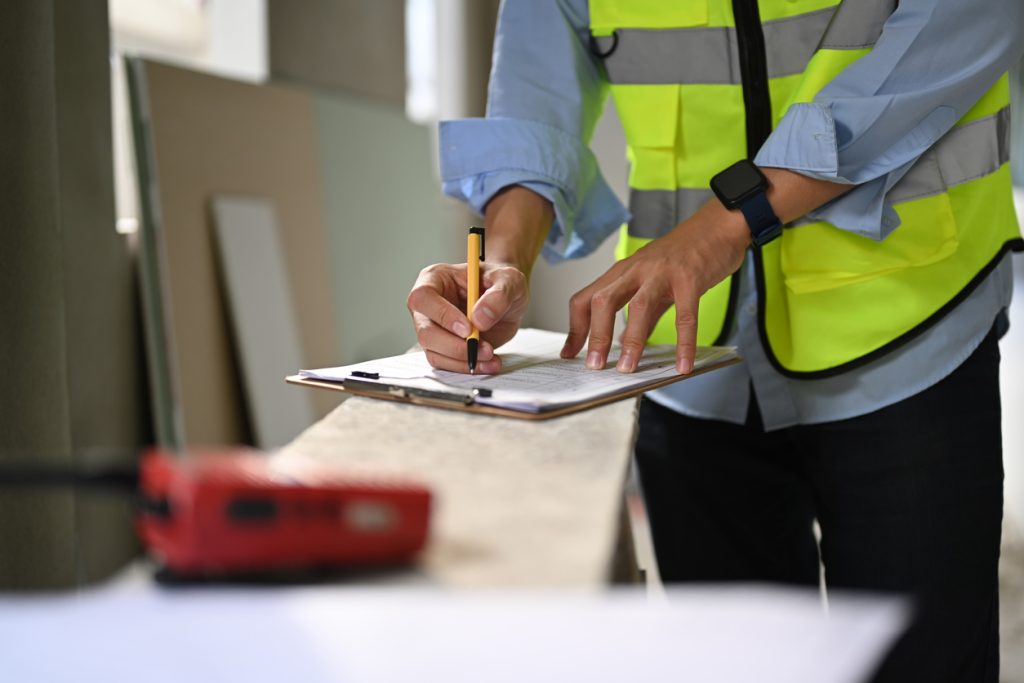 Worker in reflective vest standing and checking schedule for fire blanket inspection.